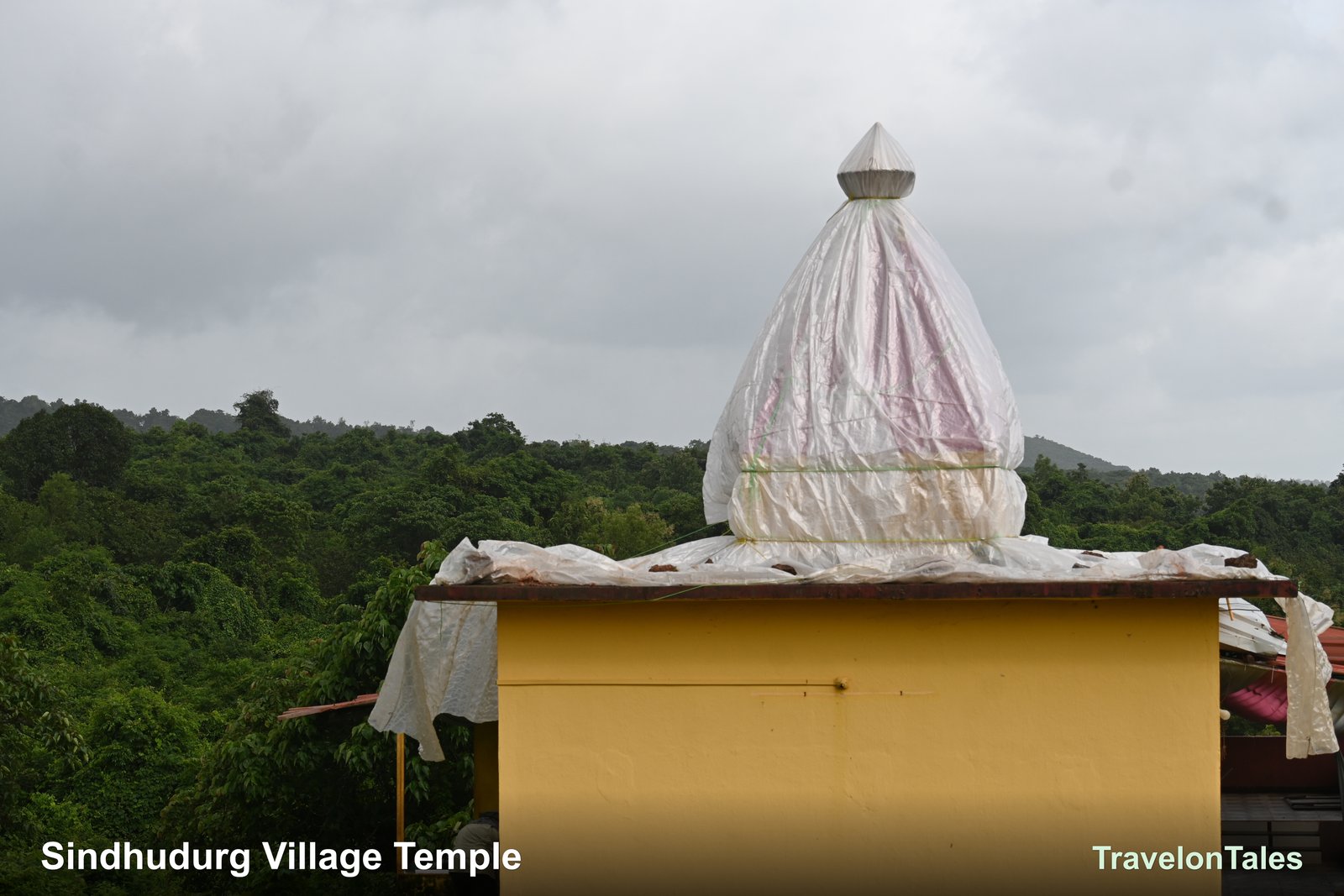 Village temple with spire wrapped in monsoon plastic, Western Ghats green hills behind — Sindhudurg, Maharashtra
